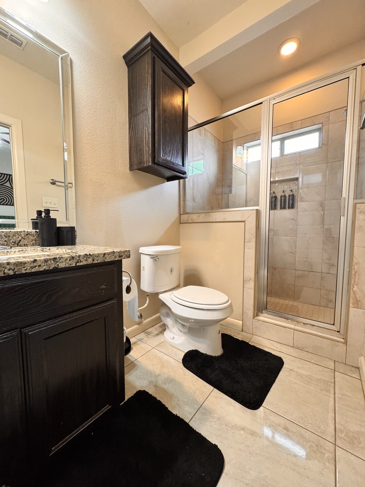 Airbnb bathroom with dark vanity, glass shower and black bath mats