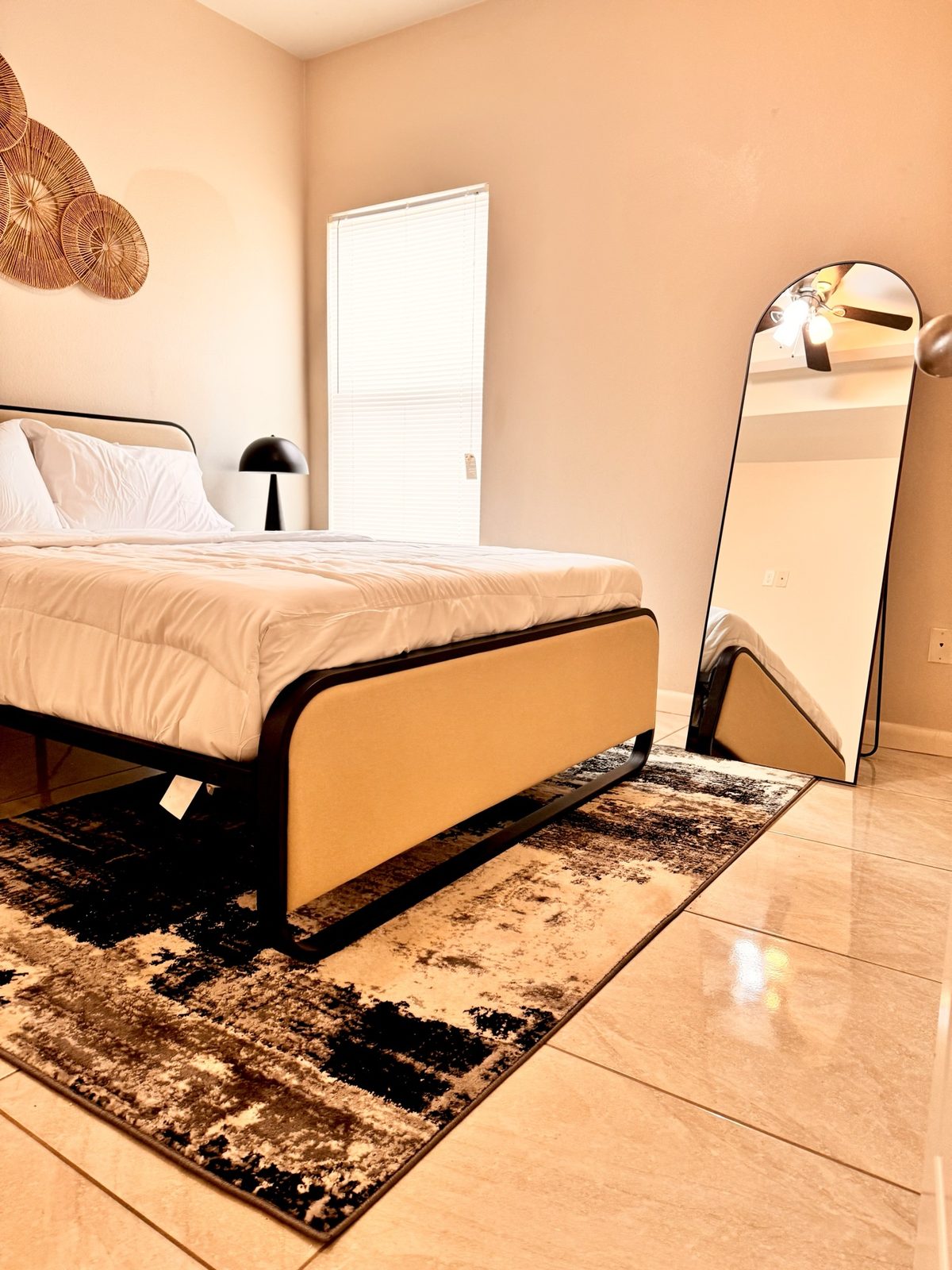 Airbnb bedroom with beige upholstered bed, arched mirror and rattan wall art