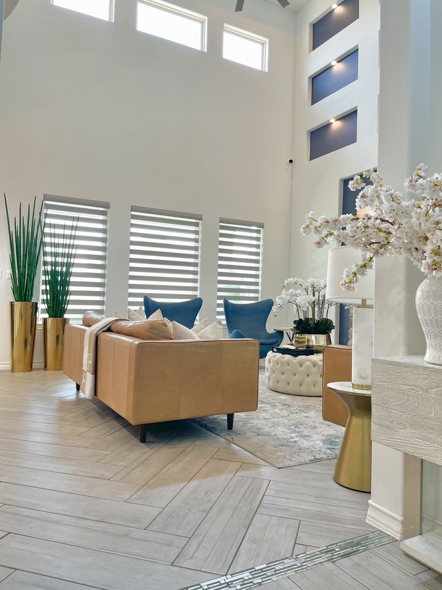 Double-height living room with cognac leather sofa, blue accent chairs and gold planters